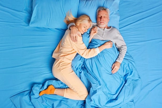 Mature couple pleasantly sleeping on sky blue bedsheets