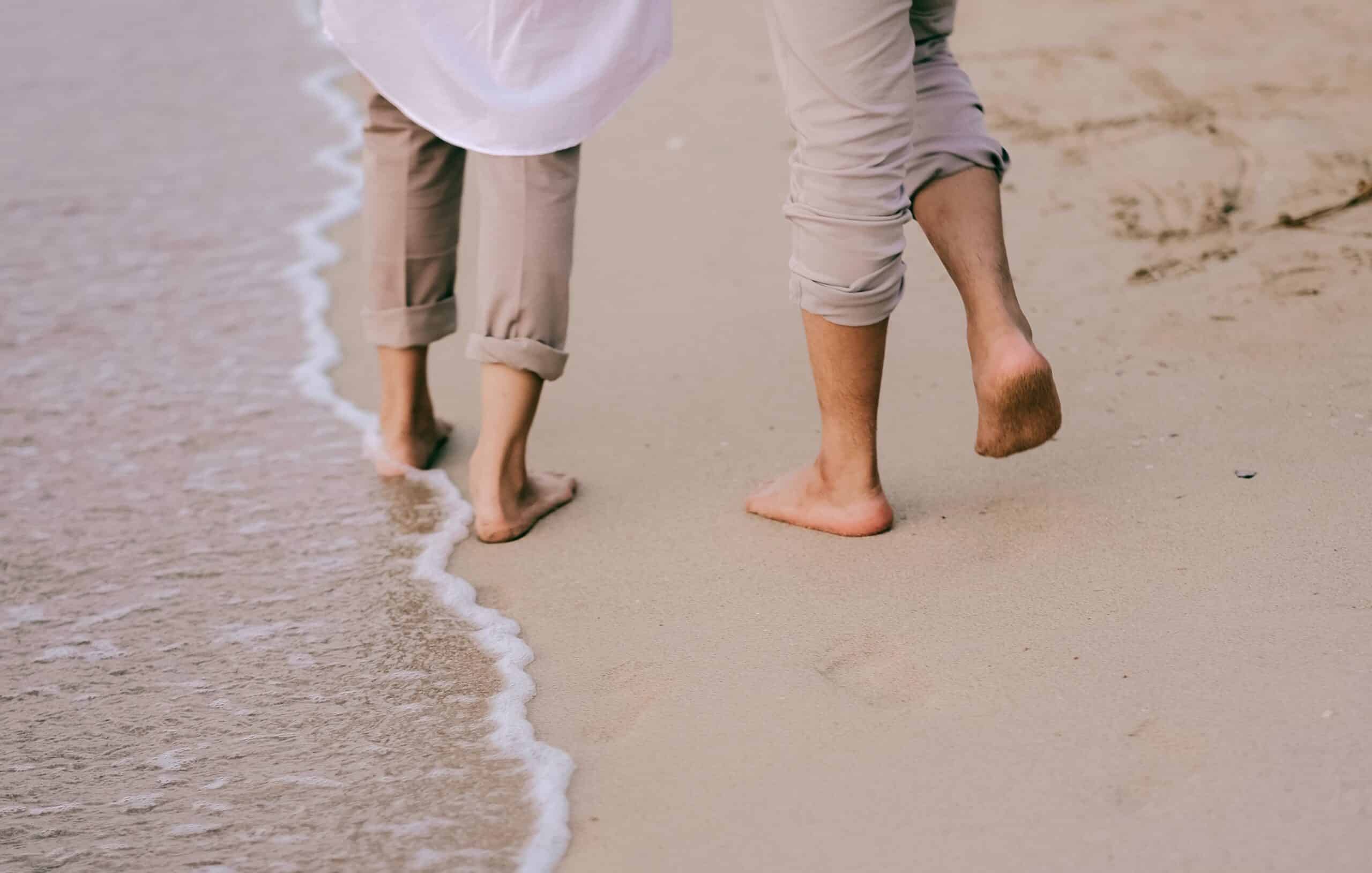 back view of two people walking barefoot on the beach for natural earthing or grounding