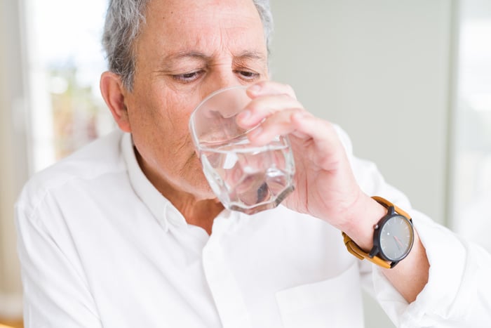 Handsome senior man drinking a fresh glass of water at home to stay hydrated for better sleep