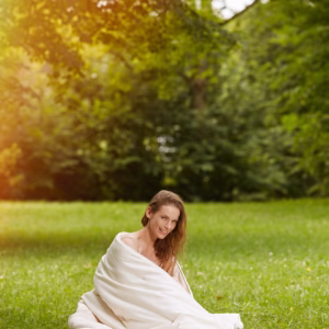 smiling woman sitting on the grass with a samina duvet wrapped around her