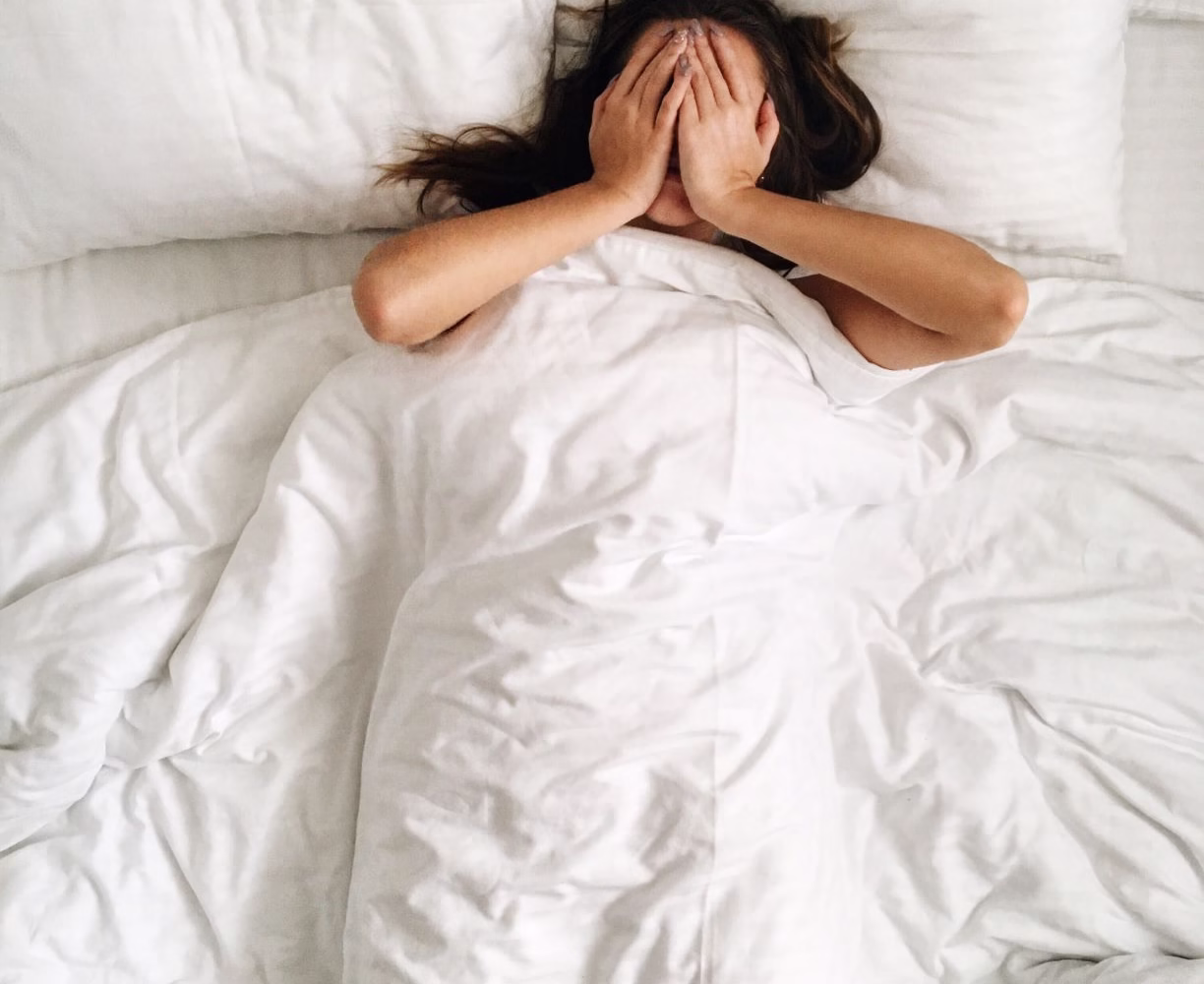 girl-in-bed-with-hands-over-eyes-blocking-light